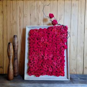 cadre de roses éternelles rouges vif poser sur une console devant un mur en bois naturel