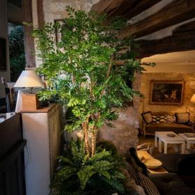 Acacia artificiel 180 cm installé dans un salon chaleureux de restaurant etoilé aux murs en pierre