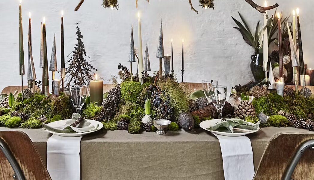 grande table de noel avec une deco vegetale centrale de mousses et pommes de pins
