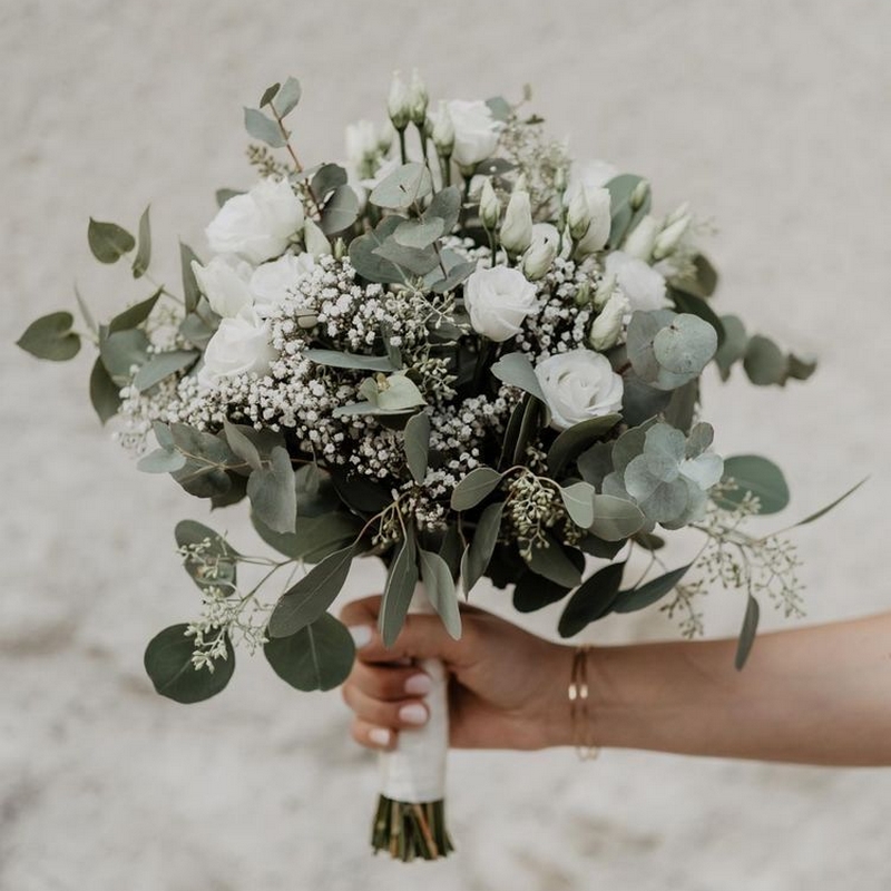 Main tenant un bouquetde mariée clair d'eucalyptus et fleurs blanches stabilisées