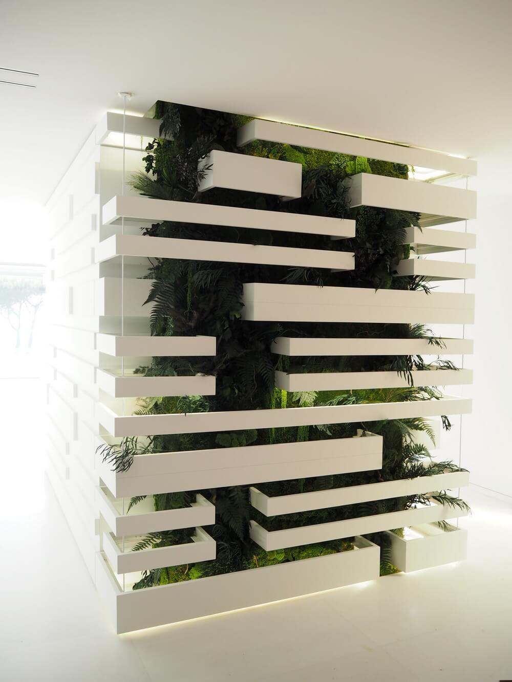 Mur végétal d'intérieur éclairé de nuit mettant en valeur le design géométrique blanc et les plantes.