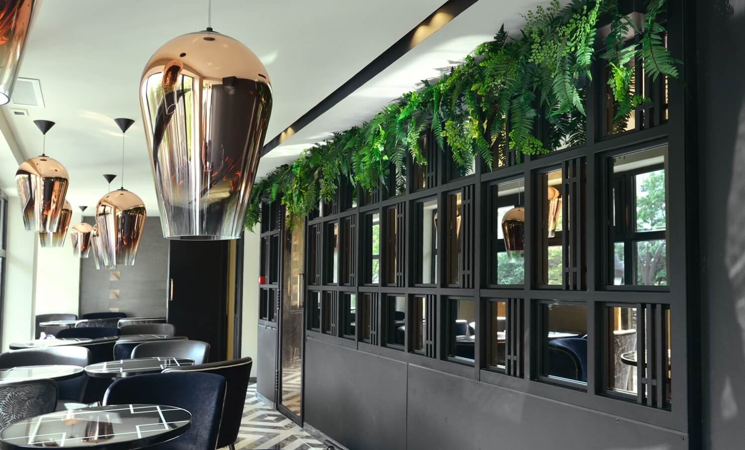 Décoration végétale d'une brasserie avec plantes suspendues au-dessus d'une verrière noire et luminaires en cuivre suspendus