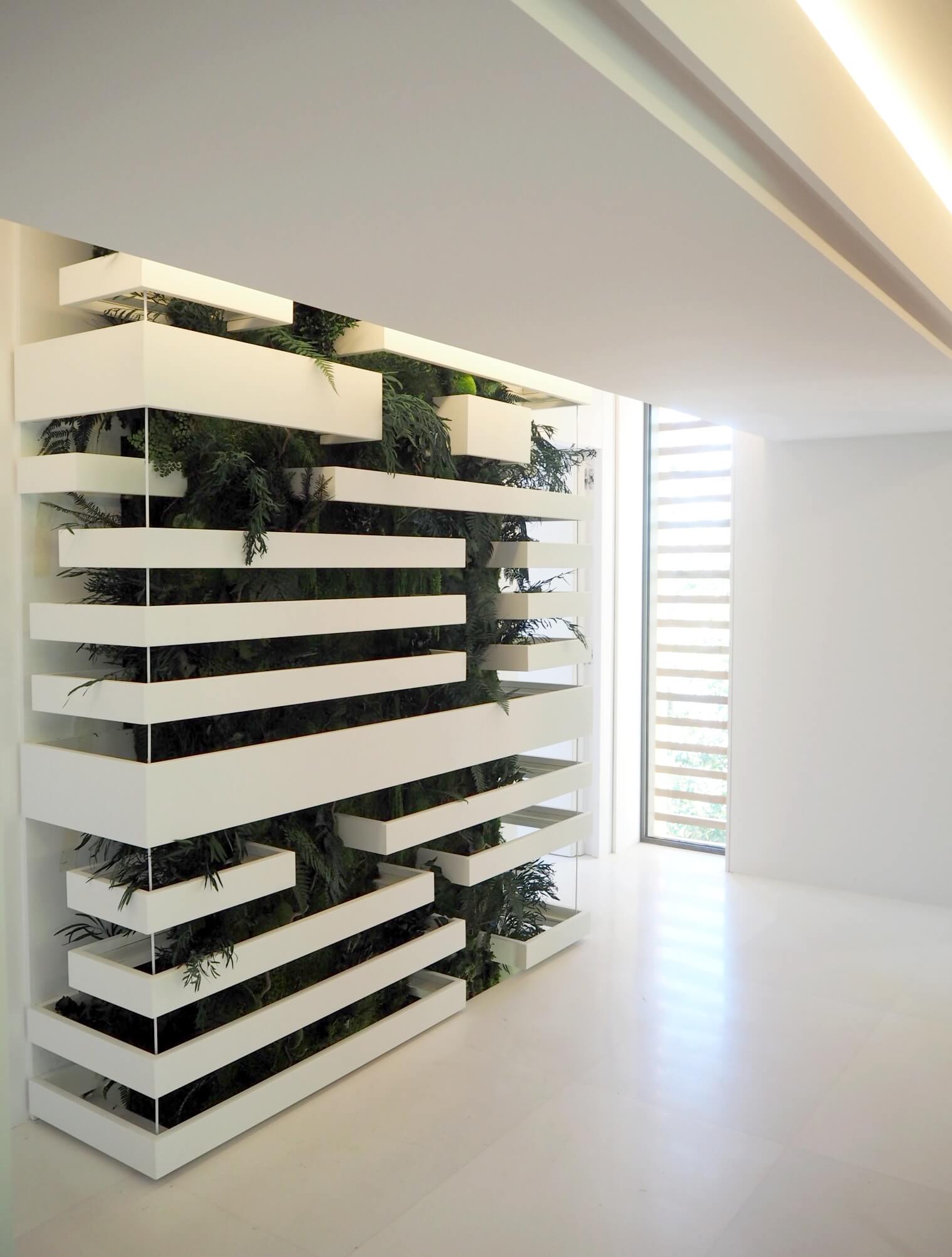 Structure métallique blanche et végétale s'étendant verticalement sur trois étages d'une maison contemporaine